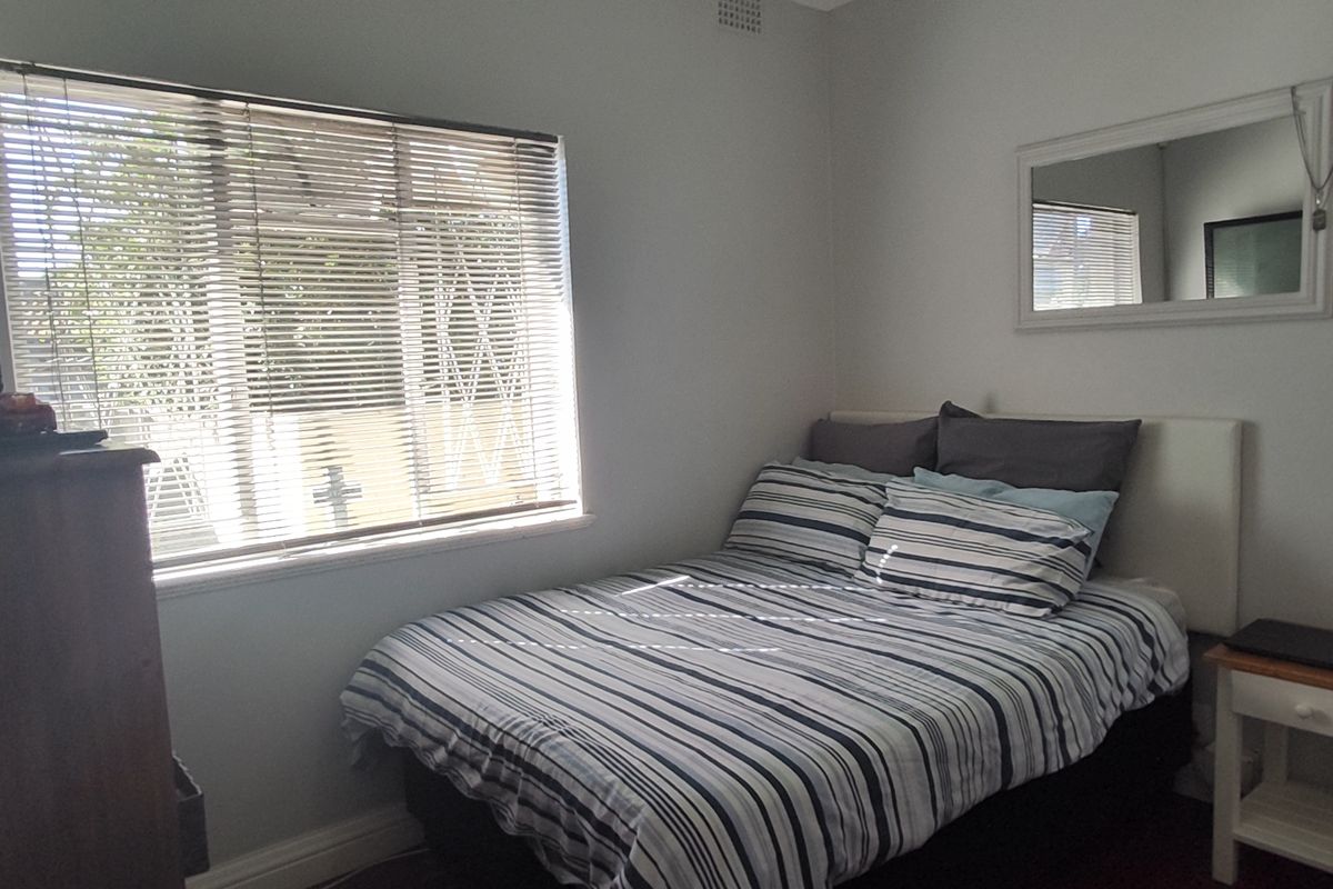 A functional bedroom featuring a window with venetian blinds and neutral wall finishes.