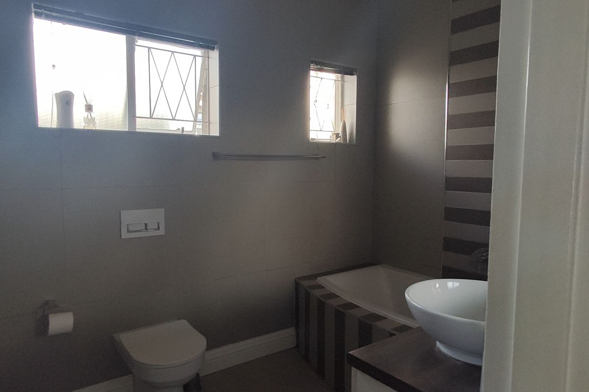A modern bathroom featuring a wall-mounted toilet, a built-in bathtub with decorative tiling, and a vessel sink set on a vanity cabinet.