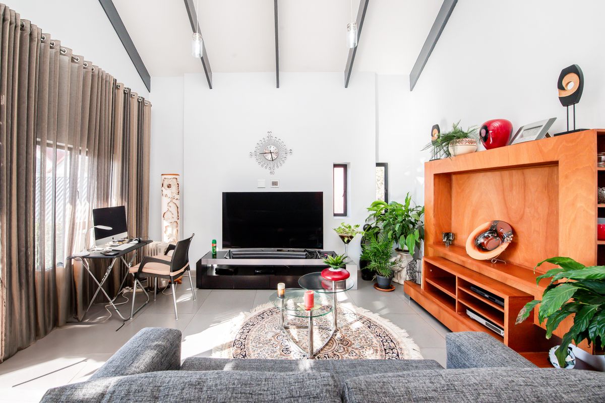 Spacious living room featuring high vaulted ceilings with exposed beams, large windows with floor-to-ceiling curtains, and tiled flooring.