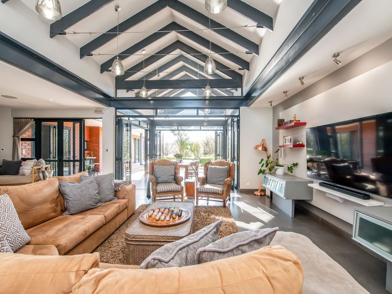 Spacious open-plan living area featuring a high vaulted ceiling with exposed beams, large glass folding doors, and modern built-in cabinetry.
