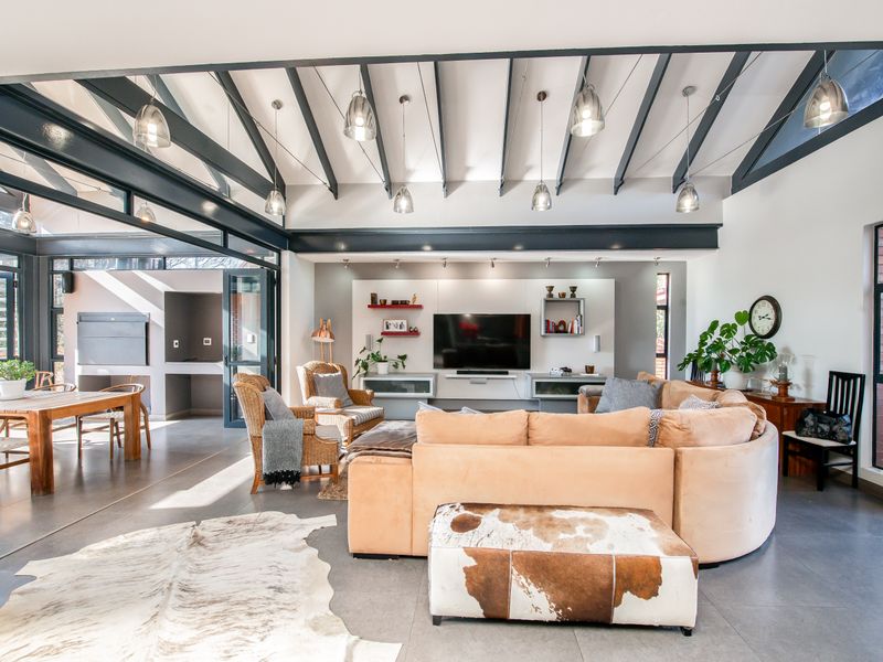 Spacious open-plan living and dining area featuring vaulted ceilings with exposed beams, large glass folding doors, and modern tiled flooring.