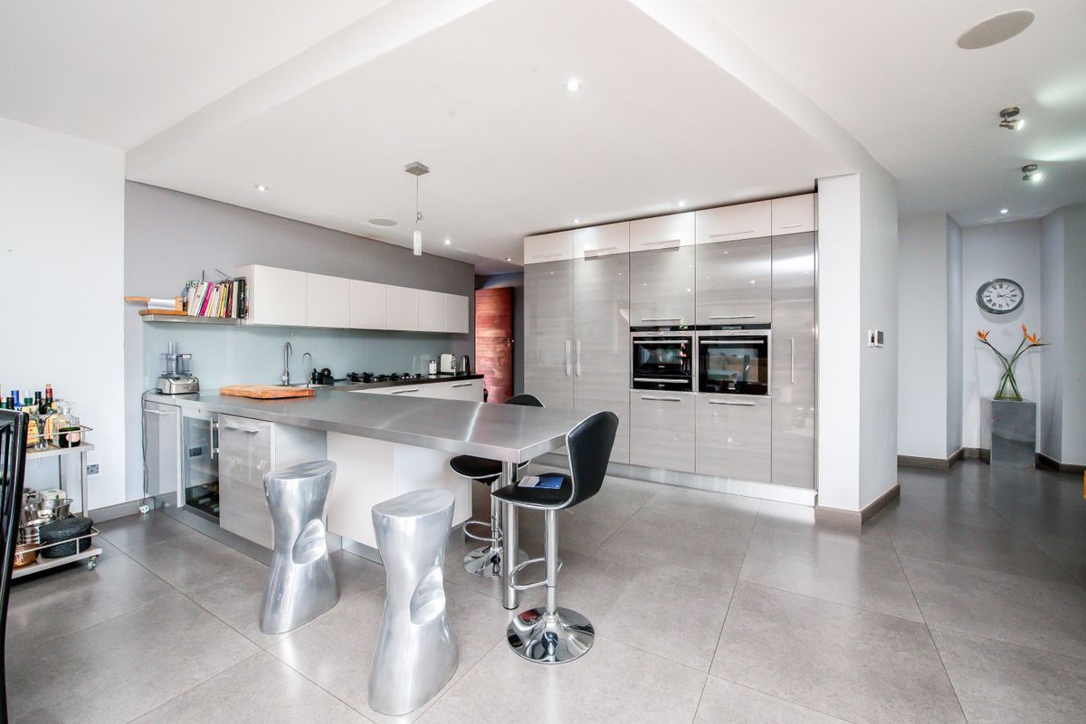 Modern kitchen featuring high-gloss cabinetry, stainless steel countertops, integrated double ovens, and a central island with breakfast bar seating.