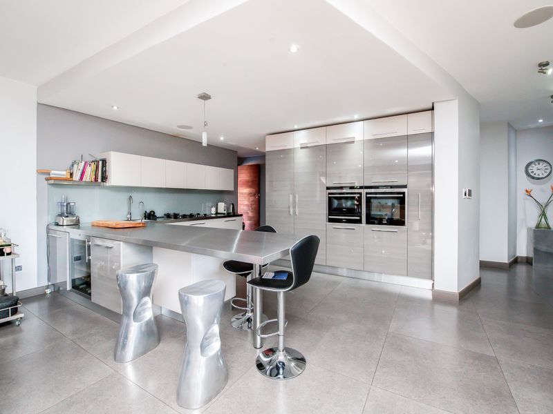Modern kitchen featuring high-gloss cabinetry, stainless steel countertops, integrated double ovens, and a central island with breakfast bar seating.