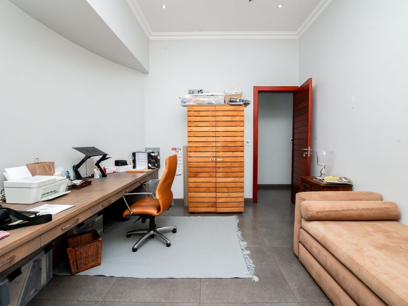 A functional home office space featuring tiled flooring, recessed ceiling lighting, and a solid timber door.