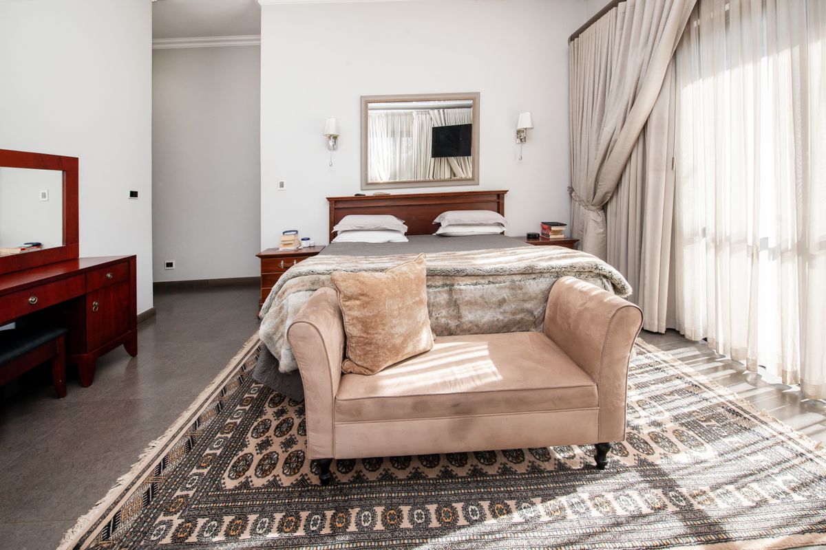 A spacious bedroom featuring tiled flooring, large floor-to-ceiling curtains, and wall-mounted lighting fixtures.