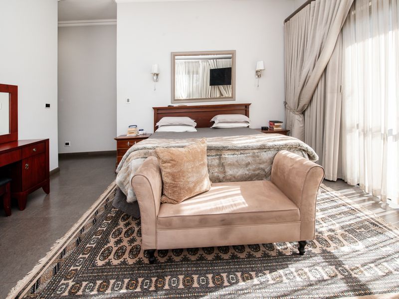 A spacious bedroom featuring tiled flooring, large floor-to-ceiling curtains, and wall-mounted lighting fixtures.
