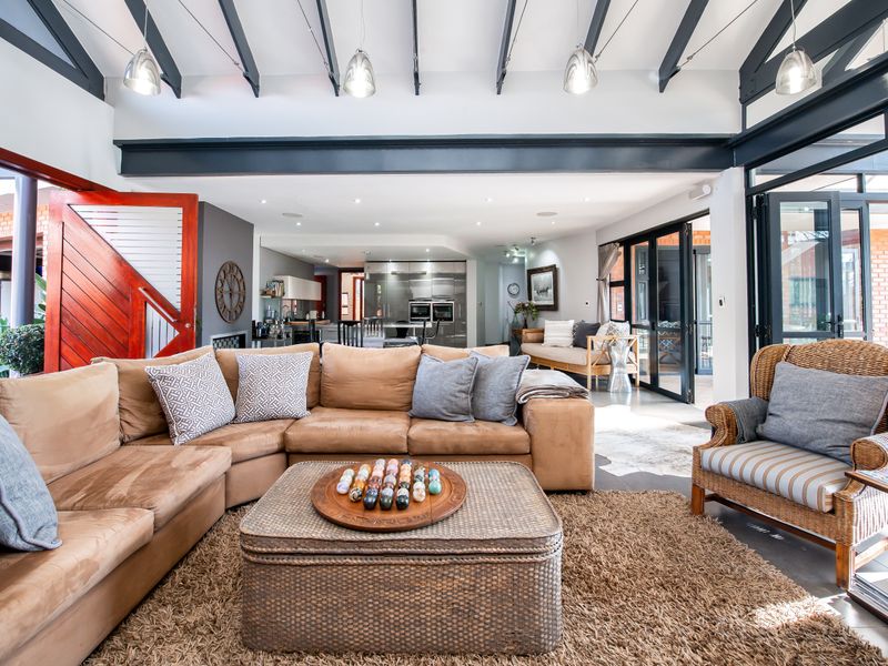 Spacious open-plan living area featuring vaulted ceilings with exposed beams, large glass sliding doors, and a seamless transition to the modern kitchen.