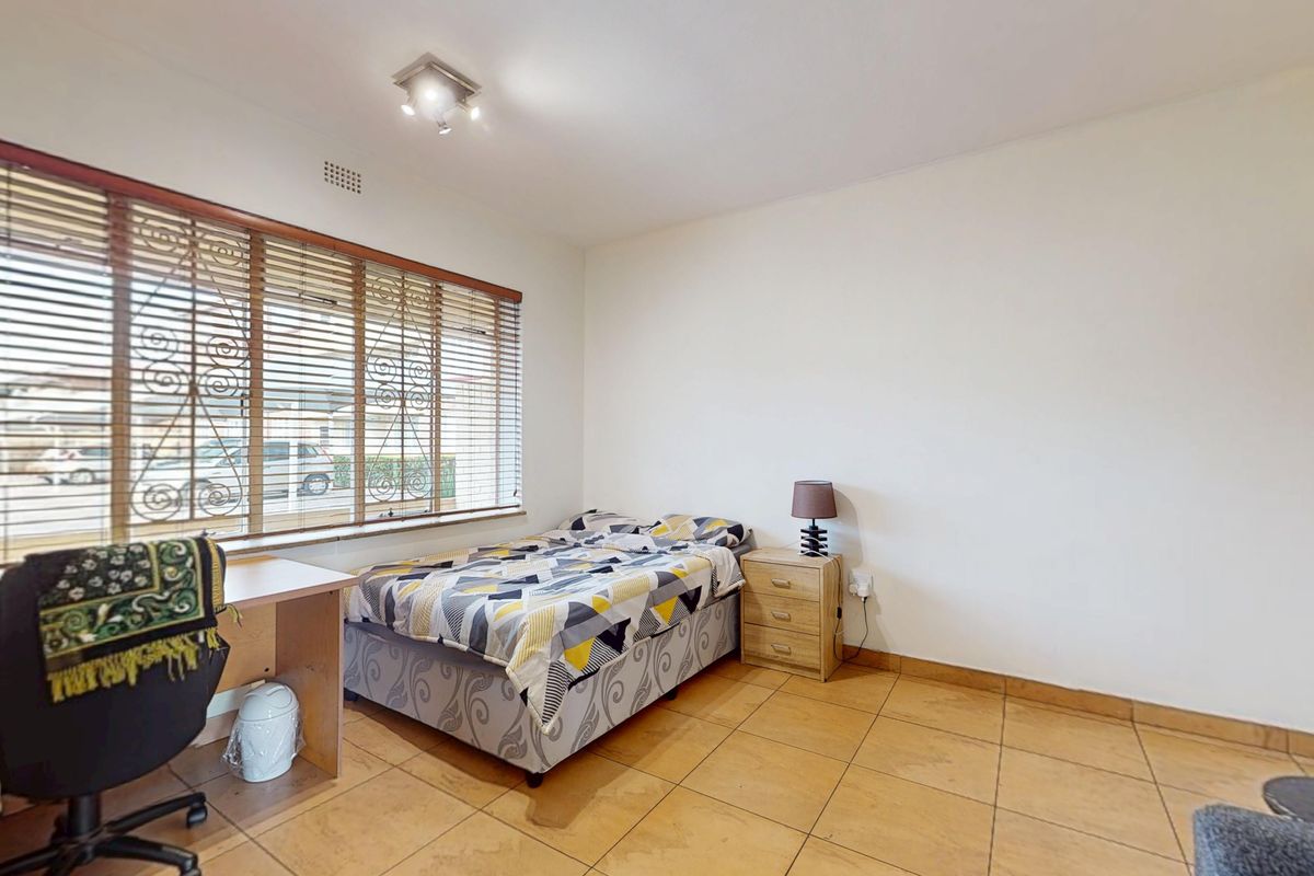A bedroom featuring tiled flooring, large windows with security bars and venetian blinds, and a central ceiling light fixture.