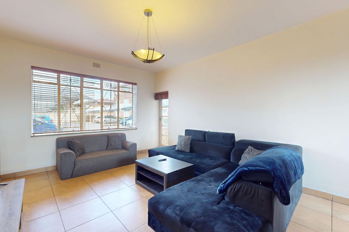 A living room featuring tiled flooring, large windows with security bars, and a central pendant light fixture.