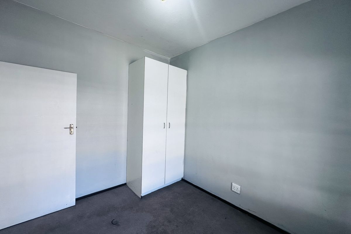 A vacant bedroom featuring neutral grey walls, carpeted flooring, and a built-in white wardrobe.