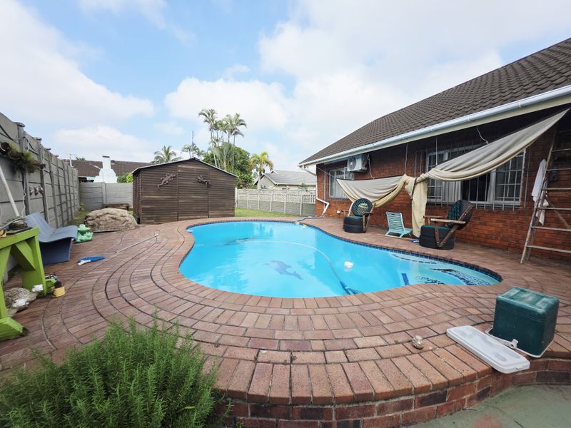 Outdoor pool area featuring a kidney-shaped swimming pool surrounded by brick paving, a precast boundary wall, and a detached timber storage shed.