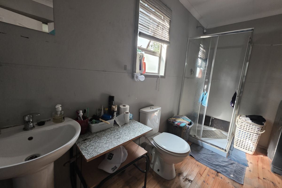A functional bathroom featuring a pedestal basin, toilet, and shower enclosure with timber flooring, currently requiring cosmetic updates and maintenance.