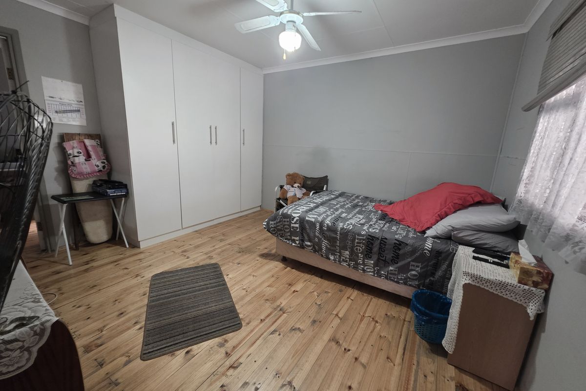 A bedroom featuring polished timber flooring, a ceiling fan, and a large white built-in wardrobe providing ample storage space.