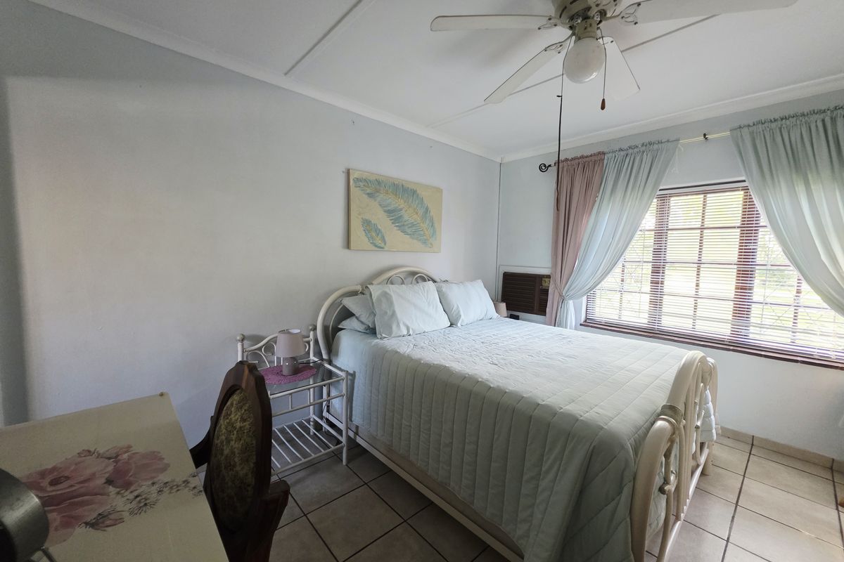 A functional bedroom featuring tiled flooring, a ceiling fan, and a built-in air conditioning unit, offering a comfortable and practical living space.