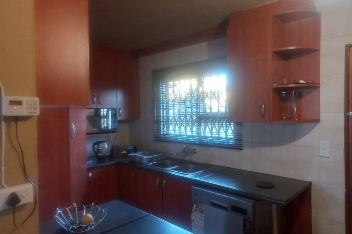 A functional kitchen featuring wood-finish cabinetry, a double-basin sink, and integrated dishwasher space, illuminated by a window with security bars.