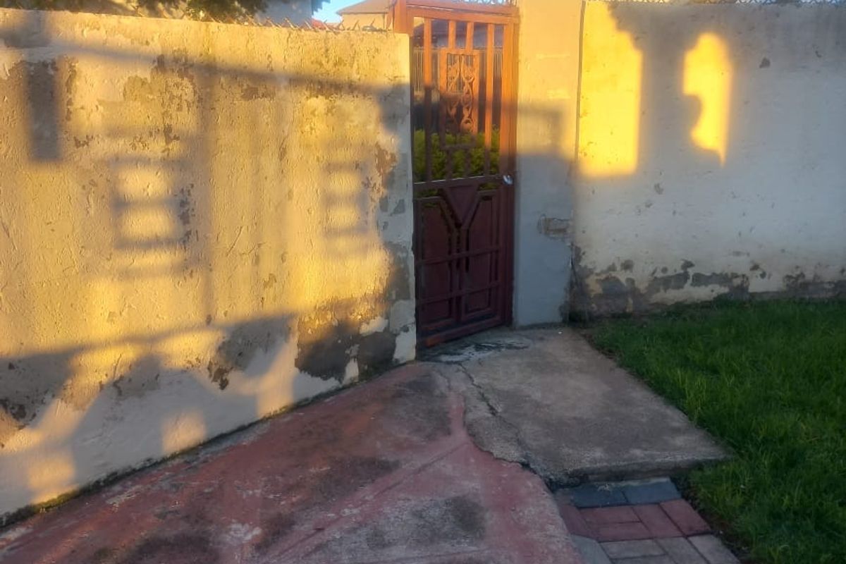 Exterior view of a side pedestrian gate with a concrete pathway and boundary wall showing signs of wear.