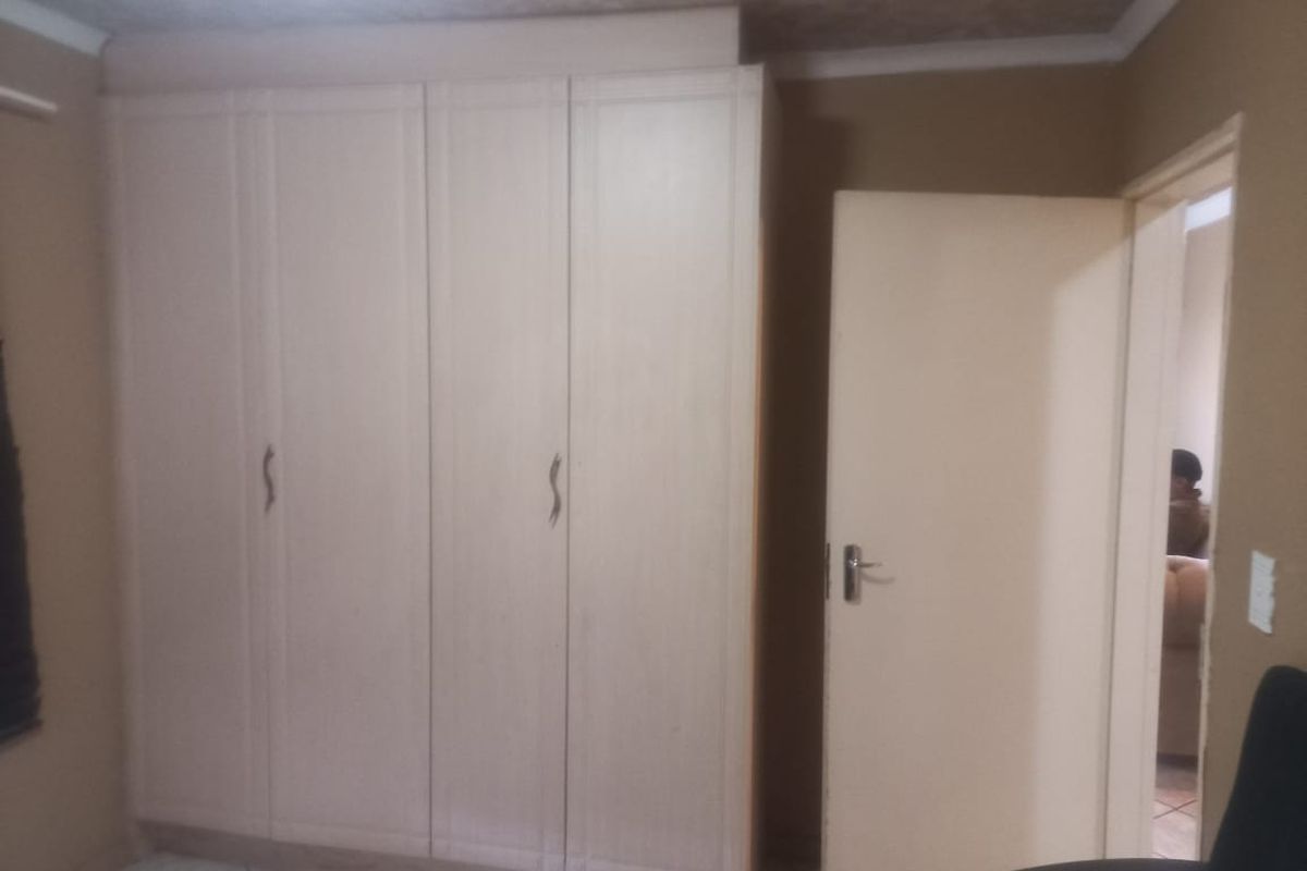 A bedroom featuring built-in wooden cupboards and tiled flooring, providing functional storage space.