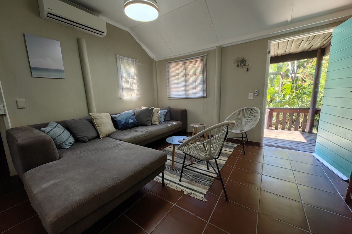 A comfortable living room featuring terracotta floor tiles, a vaulted ceiling, and a split-system air conditioner, with direct access to an outdoor patio area.