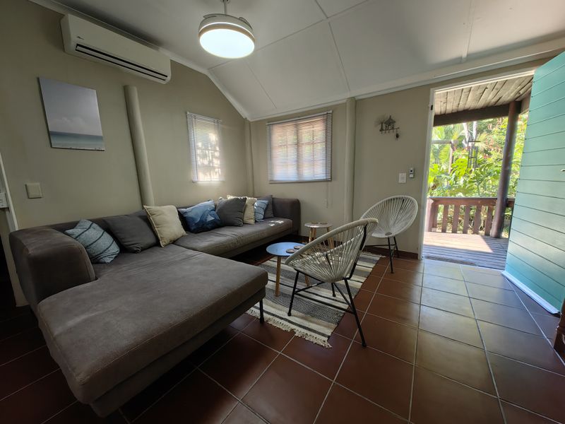 A comfortable living room featuring terracotta floor tiles, a vaulted ceiling, and a split-system air conditioner, with direct access to an outdoor patio area.