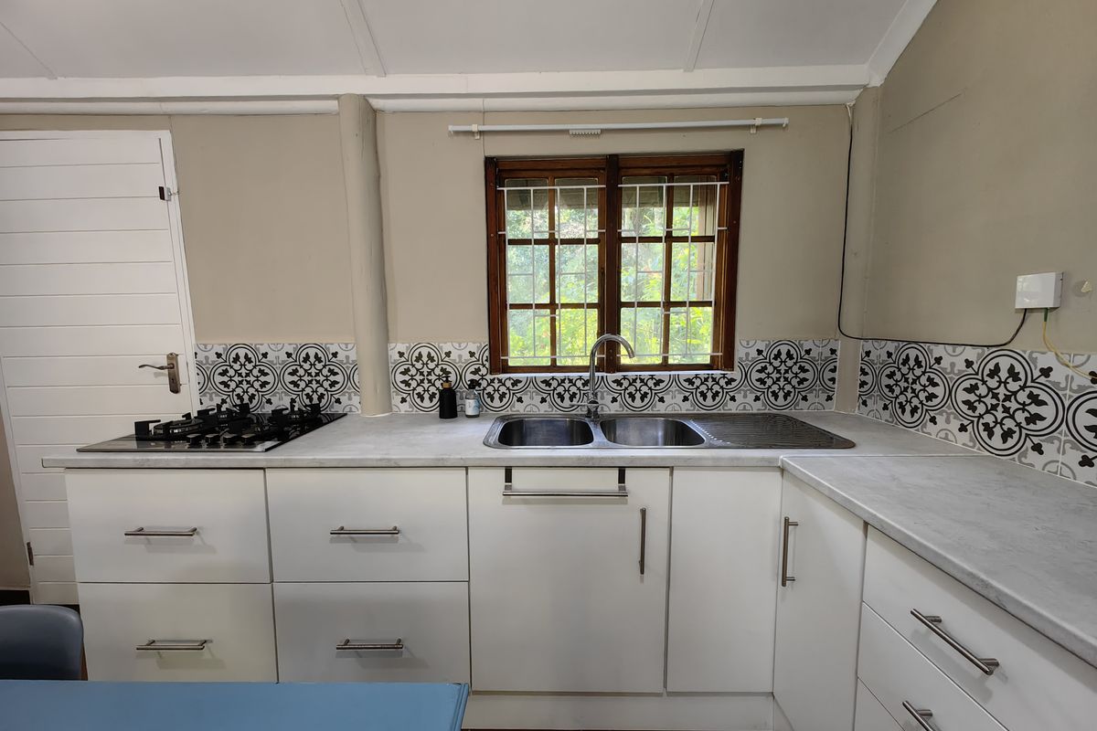A functional kitchen featuring white cabinetry, patterned tile backsplash, gas hob, and a double stainless steel sink set against a timber-framed window.
