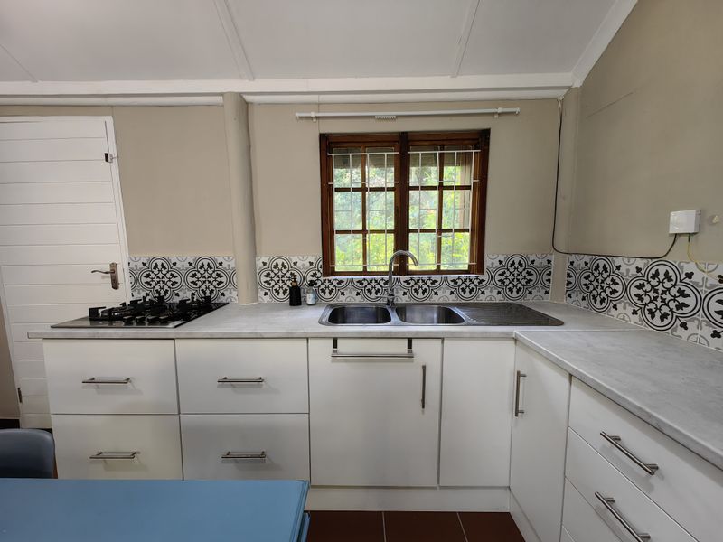 A functional kitchen featuring white cabinetry, patterned tile backsplash, gas hob, and a double stainless steel sink set against a timber-framed window.