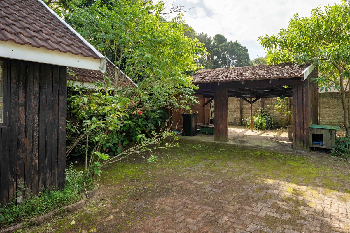 Rear garden area featuring a brick-paved courtyard, mature landscaping, and a covered timber carport structure.