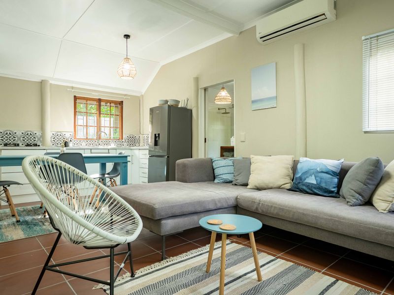An open-plan living and kitchen area featuring tiled floors, a modern kitchen with patterned backsplash, and a wall-mounted air conditioning unit.