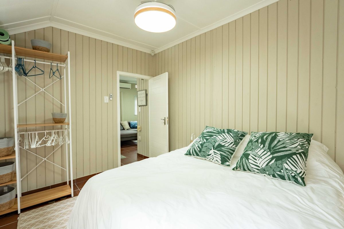 A cozy bedroom featuring vertical timber wall paneling, tiled flooring, and a central flush mount light fixture, with an adjoining room visible through the doorway.