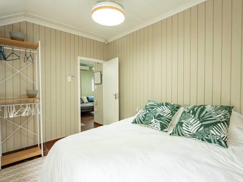 A cozy bedroom featuring vertical timber wall paneling, tiled flooring, and a central flush mount light fixture, with an adjoining room visible through the doorway.