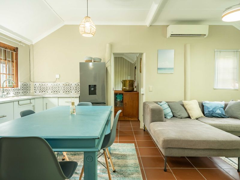 An open-plan living and kitchen area featuring vaulted ceilings, terracotta floor tiles, a modern split-system air conditioner, and a decorative tiled kitchen backsplash.