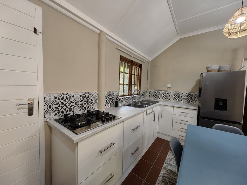 A well-maintained kitchen featuring a gas hob, double sink, decorative tiled backsplash, and ample built-in cabinetry under a vaulted ceiling.