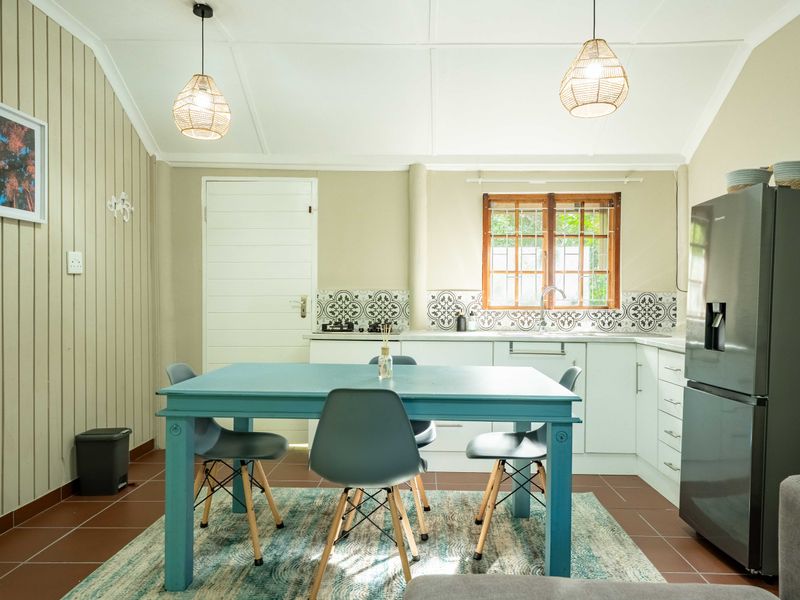 An open-plan kitchen and dining area featuring tiled floors, patterned backsplash, built-in cabinetry, and a vaulted ceiling with pendant lighting.