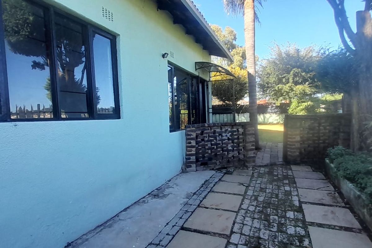 Rear exterior view of the property featuring a paved patio area, brick boundary wall, and established garden surroundings.