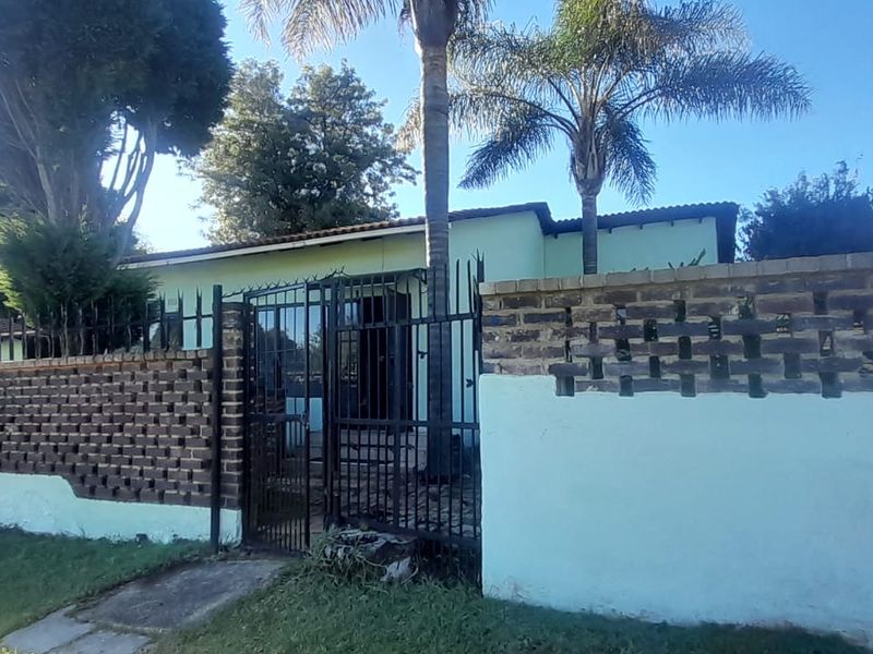 Front view of a residential property featuring a brick boundary wall, metal security gate, and established garden area.
