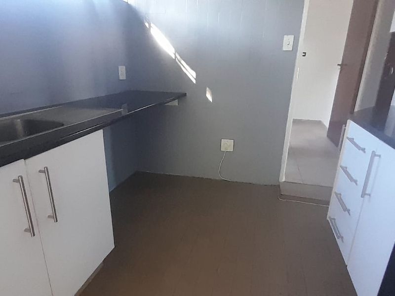 A functional kitchen space featuring white cabinetry, dark countertops, and a stainless steel sink, currently vacant and ready for updates.