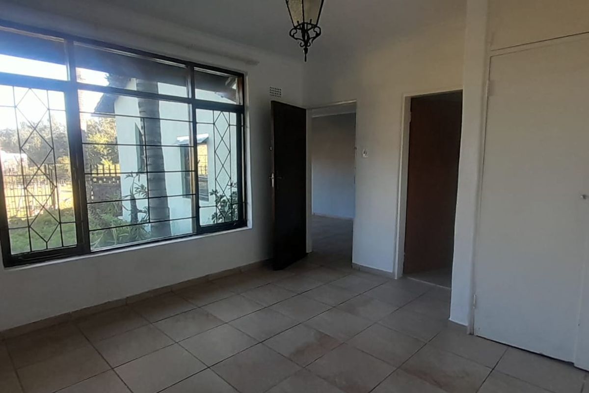 An empty bedroom featuring tiled flooring, built-in cupboards, and a large window with security bars, offering a blank canvas for personalization.