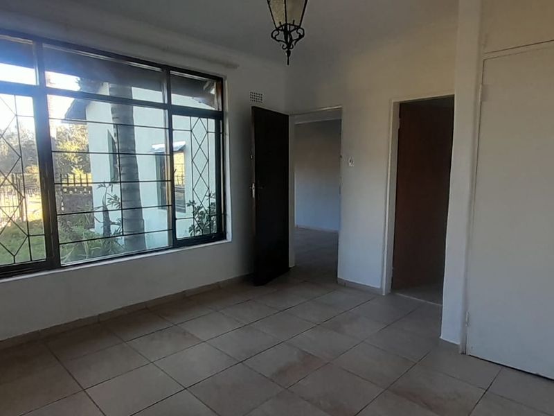 An empty bedroom featuring tiled flooring, built-in cupboards, and a large window with security bars, offering a blank canvas for personalization.