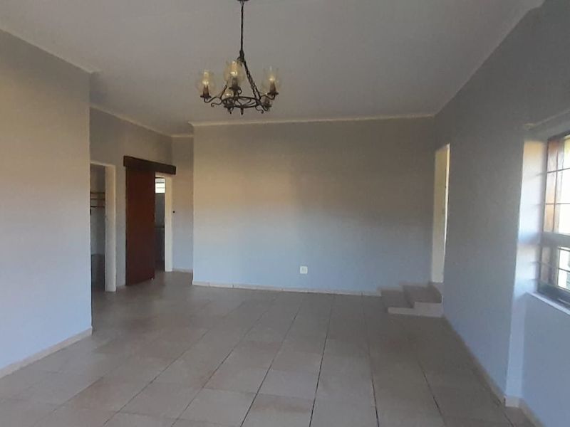 A spacious, empty living area featuring neutral wall tones, tiled flooring, and a classic wrought iron chandelier, offering a blank canvas for interior design.