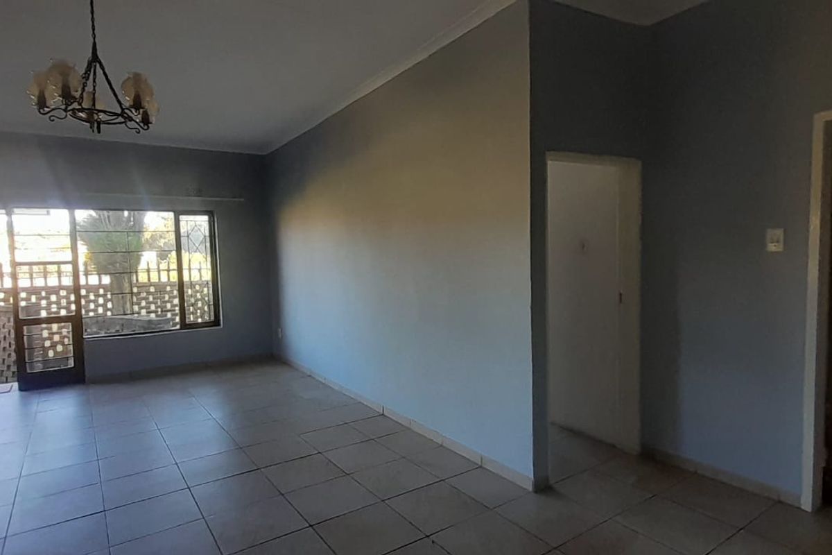 Spacious, empty living area featuring neutral tiled flooring, cove cornicing, and a large sliding glass door providing access to the exterior.