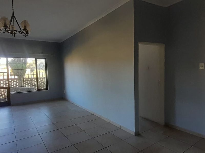 Spacious, empty living area featuring neutral tiled flooring, cove cornicing, and a large sliding glass door providing access to the exterior.