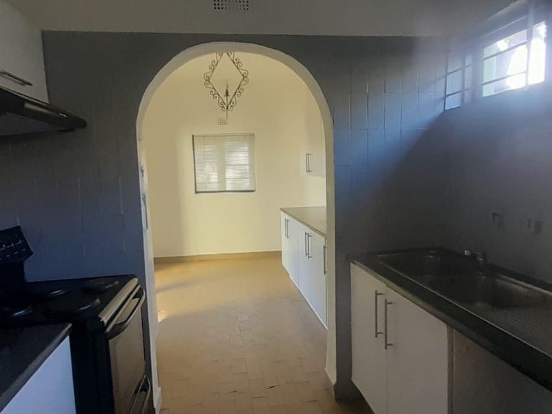 A functional kitchen featuring built-in cabinetry, a stainless steel sink, and an electric stove, leading through an arched doorway into an adjacent space.