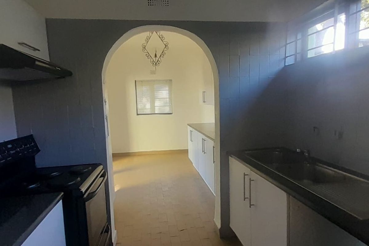 A functional kitchen featuring built-in cabinetry, a stainless steel sink, and an electric stove, leading through an arched doorway into an adjacent space.