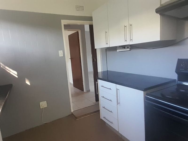 A functional kitchen featuring white cabinetry, dark countertops, a freestanding stove with extractor fan, and tiled flooring.