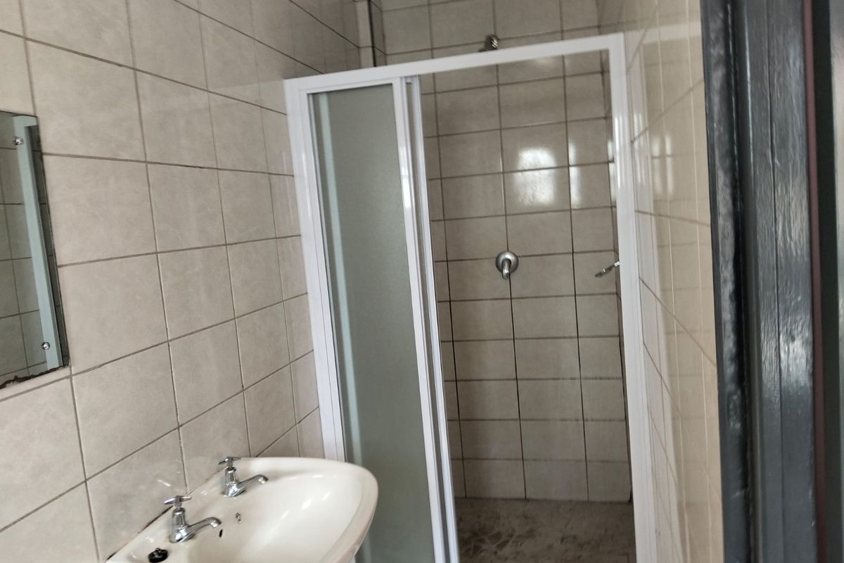 A functional bathroom featuring a shower enclosure with a sliding door and a wall-mounted basin.