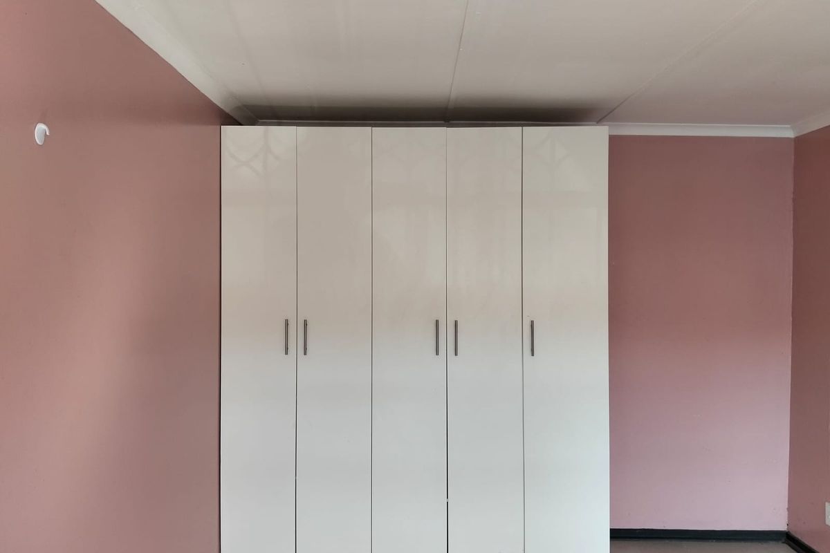 A bedroom featuring built-in white cabinetry with modern handles against pink painted walls and tiled flooring.