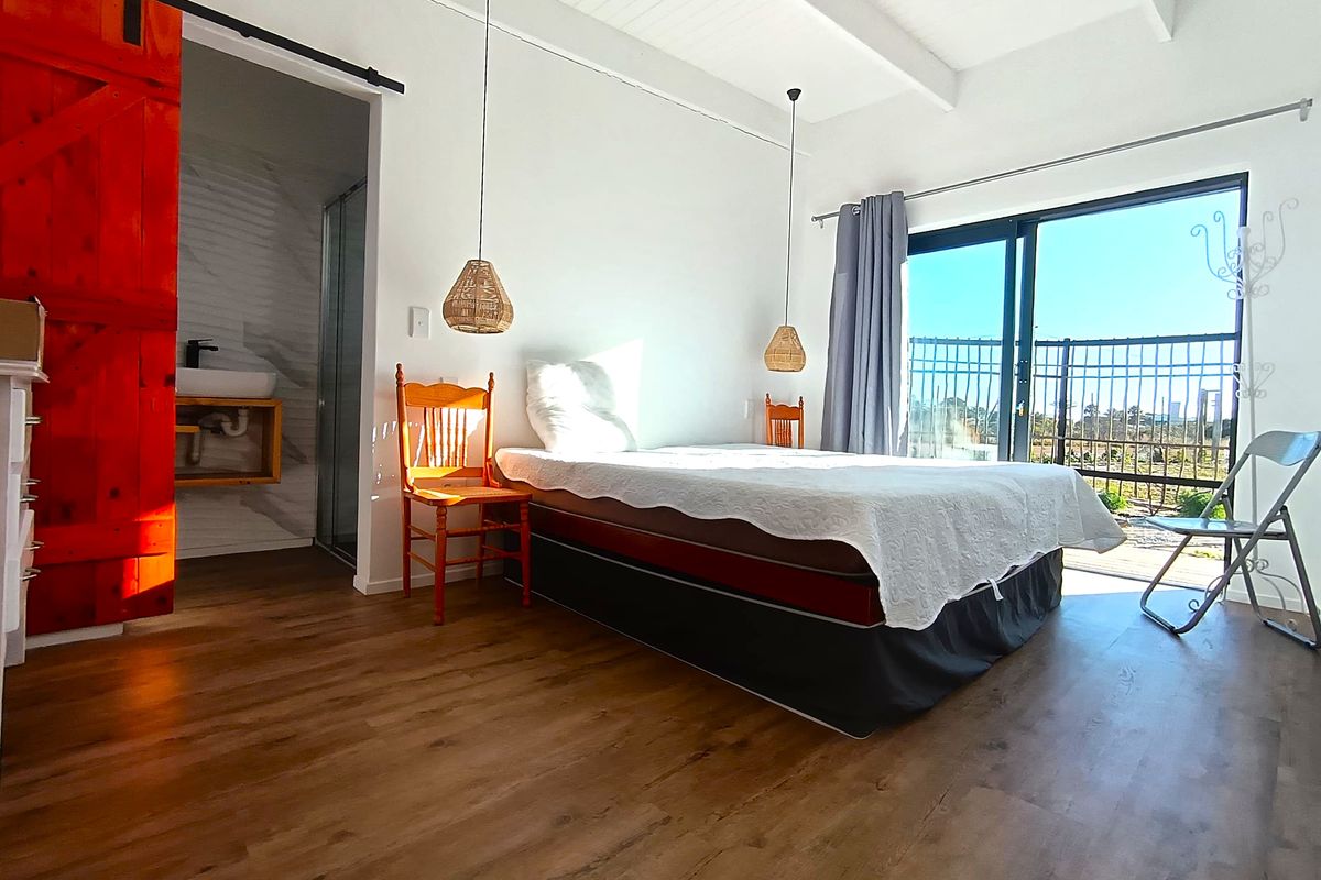 Bright bedroom featuring exposed beam ceilings, laminate flooring, a vibrant red sliding barn door, and direct access to an en-suite bathroom and outdoor area.