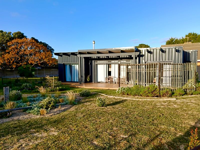 Rear view of a modern home featuring metal cladding, timber decking, and a landscaped garden with a wooden fence.