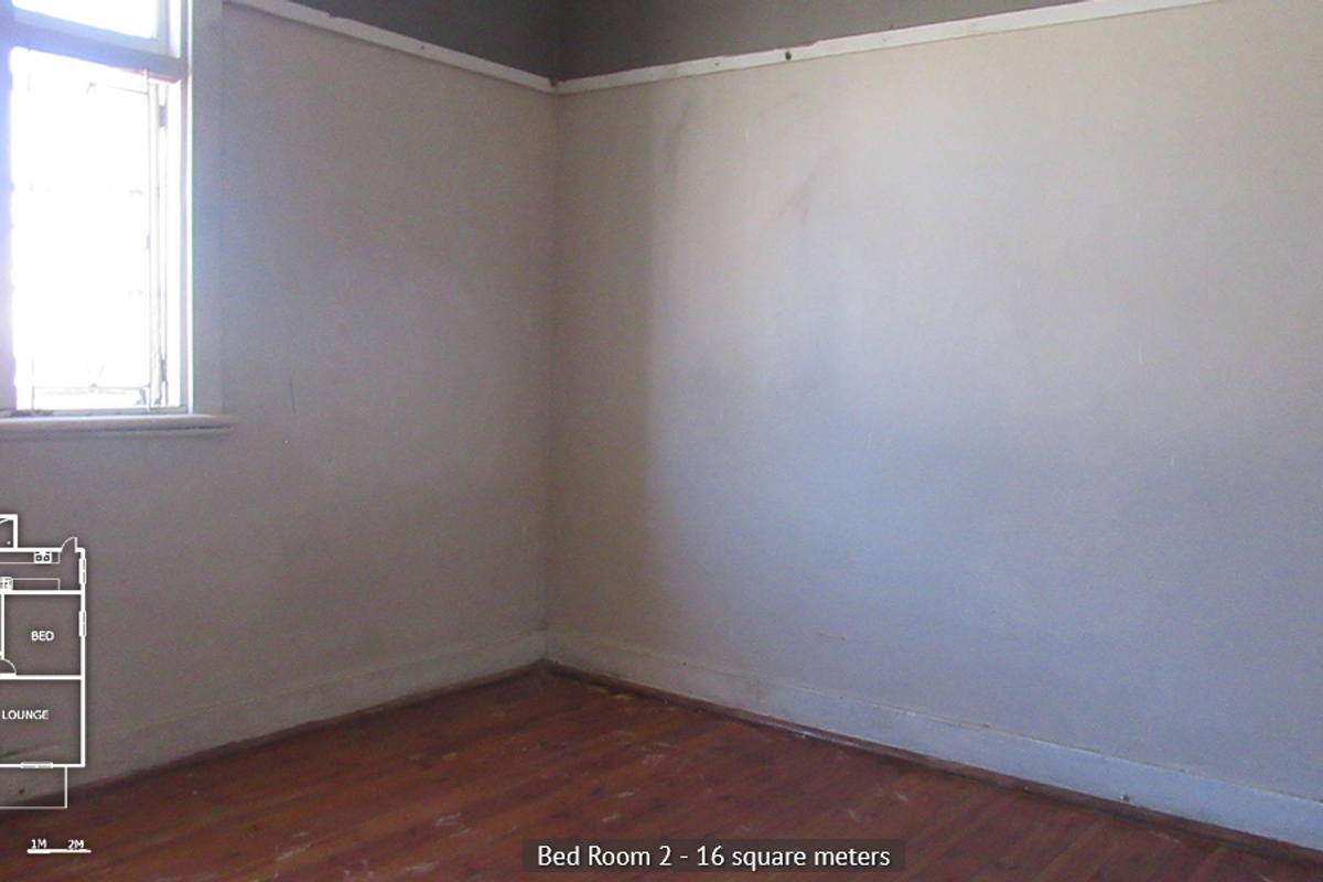 An empty bedroom featuring original timber flooring, a casement window, and a picture rail, requiring cosmetic updates to the walls and floors.