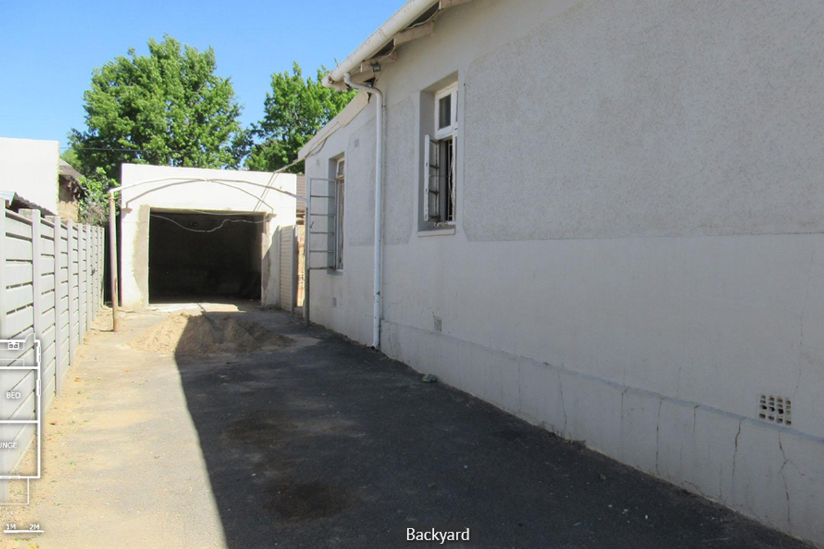 Rear exterior view showing a paved driveway, boundary wall, and detached garage structure with visible exterior wall maintenance required.