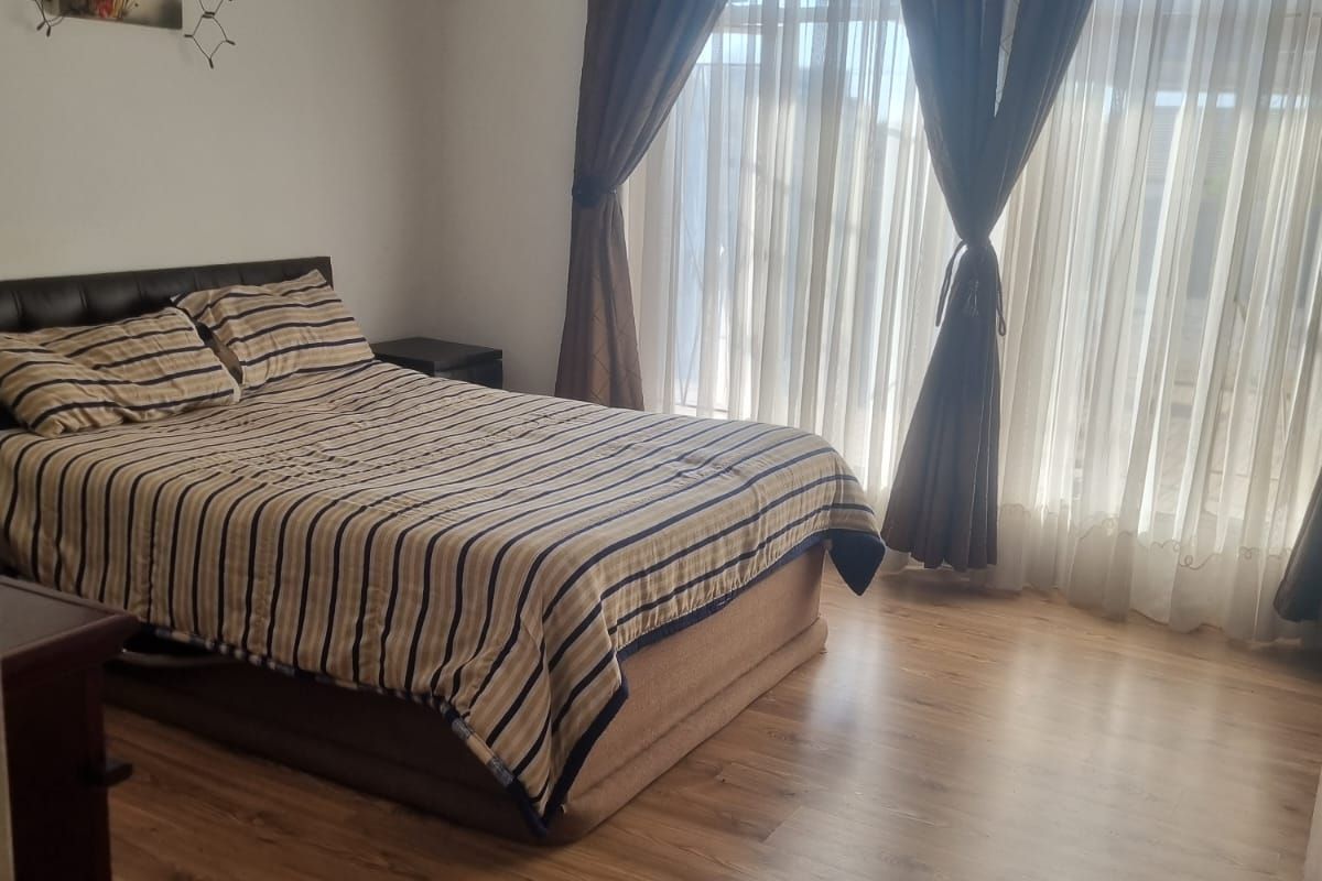 A bedroom featuring laminate flooring and large windows with curtain treatments, offering a functional and neutral space.